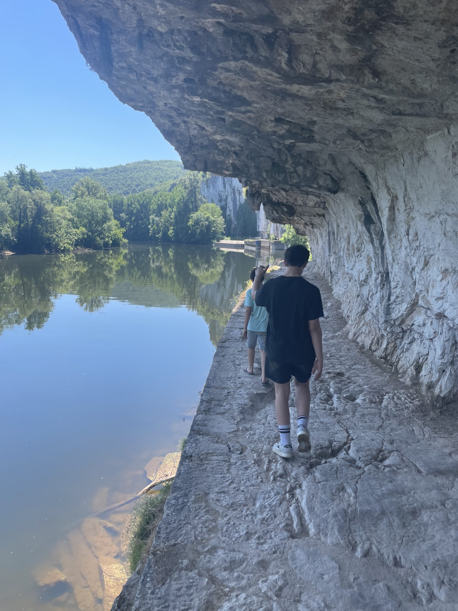Promeneur sur un chemin au bord de l’eau, sous une falaise calcaire